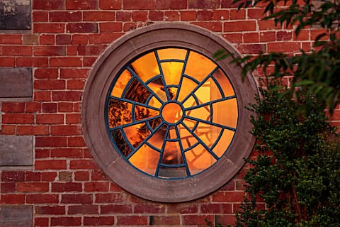 MORTON_HALL_WORCESTERSHIRE_WEST_GARDEN_SUNSET_ROUND_WINDOW_ON_WALL_WITH_SUNSET_REFLECTED_IN_GLASS