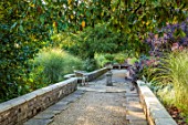 BOWCLIFFE HALL, YORKSHIRE: DESIGN ALISTAIR BALDWIN: PATH, STONE URN, CONTAINER, WOODEN BENCH, SEAT, MISCANTHUS MORNING LIGHT, COTINUS, SEPTEMBER