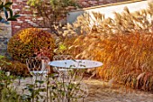 THE OLD RECTORY, QUINTON, NORTHAMPTONSHIRE: DESIGNER ANOUSHKA FEILER: MISCANTHUS SINENSIS KLEINE FONTAINE, WHITE METAL TABLE, CHAIRS, GRASSES, AUTUMN, FALL, CLIPPED FAGUS SYLVATICA