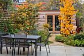 SMALL LONDON GARDEN DESIGNED BY ALASDAIR CAMERON: NOVEMBER, WOODLAND, TREES, PARROTIA PERSICA, PERSIAN IRONWOOD TREE, SHED, PATH, BARBEQUE, BBQ, FIRE, FALL, AUTUMN, TABLE, PATIO