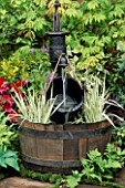 HALF BARREL WITH WATER PUMP AND BUCKET WITH VARIEGATED IRIS LEAVES.   CHELSEA 95