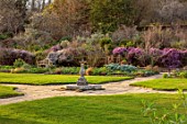 GRAVETYE MANOR, SUSSEX: LAWN, SUNDIAL AND PINK FLOWERS OF HEATHERS, SPRING, MARCH, EVENING LIGHT