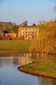 PRIORS MARSTON, WARWICKSHIRE, THE MANOR HOUSE: WILLOW ON AN ISLAND IN THE LAKE WITH MANOR HOUSE IN THE BACKGROUND, MARCH