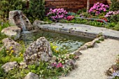 CHELSEA 2022: A SWISS SANCTUARY BY LILLY GOMM: METAL SEAT, BENCH, RHODODENDRONS, GRAVEL PATHS, ROCKS, WATERFALL, POOL, POND. PINES, FENCE, FENCING