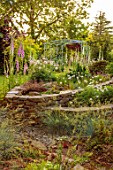 LITTLE ASH BUNGALOW, DEVON: LAWN, RAISED STONE BEDS WITH DIGITALIS, FOXGLOVES, PINK AND WHITE FLOWERED, ARCH, GRAVEL