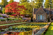 THE SUMMERHOUSE, OXFORDSHIRE: JULY, SUMMER, VIEW ALONG CANAL, POND, POOL, WATER, GARDEN TO HOUSE, BORDERS, YEW PYRAMIDS, MAPLES, TREES, WATERLILIES, REFLECTIONS, COTSWOLDS