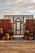 ORDNANCE HOUSE, WILTSHIRE: COUNTRY GARDEN, FROST, FROSTY, WINTER, SUNRISE, DAWN, BEECH HEDGES, HEDGING, GREENHOUSE, GLASSHOUSE, GRAVEL, GATE, TERRACOTTA CONTAINERS, BOX BALLS