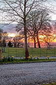 MORTON HALL GARDENS, WORCESTERSHIRE: SUNSET, WEST, TREES, LAWN, BORROWED LANDSCAPE, FENCES, FENCING, DAFFODILS