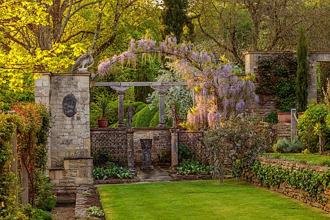 IFORD_MANOR_WILTSHIRE_MAY_SPRING_PURPLE_FLOWERS_OF_WISTERIA_OVER_ARCH_AT_THE_WEST_END_OF_TERRACE_LAW