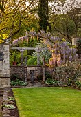 IFORD MANOR, WILTSHIRE: MAY, SPRING, PURPLE FLOWERS OF WISTERIA OVER ARCH AT THE WEST END OF TERRACE, LAWN, PAIR OF ITALIAN DANCING FIGURES