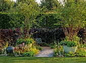HAMPTON COURT 2023: DESIGNER LUCY TAYLOR, TRADITIONAL TOWNHOUSE GARDEN, STONE PATH, METAL SEATS, DECORATIVE CONTAINERS WITH MULTISTEMMED PRUNUS SERRULA