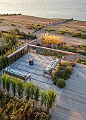 SEASIDE GARDEN , KENT: DESIGNER DECLAN BUCKLEY: VIEW ON TO DECKING, STONE TERRACE, WOODEN BENCH, SEAT, SEATING AREA, CUSHIONS, AUGUST, BARBEQUE, BARBECUE