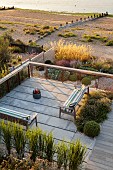 SEASIDE GARDEN , KENT: DESIGNER DECLAN BUCKLEY: VIEW ON TO DECKING, STONE TERRACE, WOODEN BENCH, SEAT, SEATING AREA, CUSHIONS, AUGUST, BARBEQUE, BARBECUE