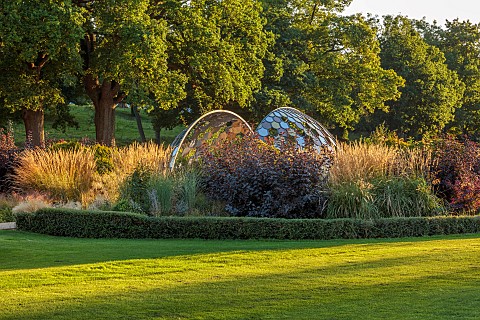 GRANTLEY_HALL_YORKSHIRE_SUNSET_LAWN_BORDERS_GRASSES_PATINATED_STEEL_AND_COLOURED_STAINLESS_STEEL_GLA