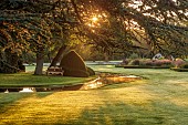 GRANTLEY HALL, YORKSHIRE: LAWN, YEWS, ISLAND, POOL, WATER, STEPPING STONES, DAWN, SUNRISE, TREES, MIST, FOG, WOODEN BENCH, SEAT, GRASSES