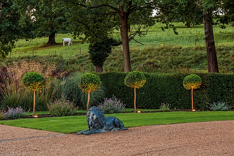 GRANTLEY_HALL_YORKSHIRE_LIGHTING_LION_STATUE_BY_PATH_DRIVE_LOLLIPOP_TOPIARY_YEW_HEDGES_HEDGING_BORRO