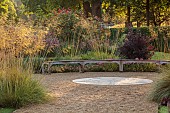 GRANTLEY HALL, YORKSHIRE: GRAVEL GARDEN, CURVED WOODEN SEAT, BENCH, A PLACE TO SIT, STIPA GIGANTEA, WOODS, TREES