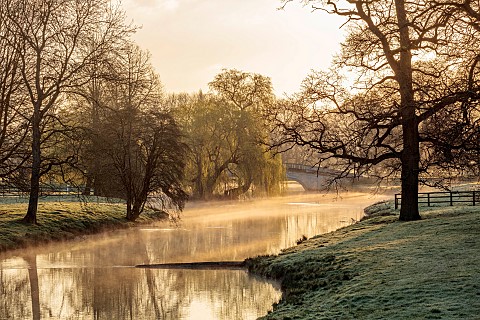 COTTESBROOKE_HALL_AND_GARDENS_NORTHAMPTONSHIRE_THE_MITCHELL_BRIDGE_WATER_LAKE_SUNRISE_MARCH_SPRING