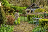 CAISSON GARDEN, SOMERSET: SPRING, MARCH, GATE, TERRACE WITH TABLE AND CHAIRS, WALL WITH TERRACOTTA CONTAINERS PLANTED WITH TULIP GAVOTA