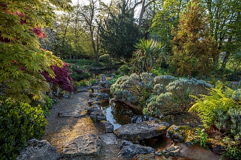 DODDINGTON_PLACE_KENT_APRIL_SPRING_THE_ROCK_GARDEN_STREAM_ACERS_YUCCA