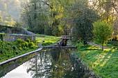 CAISSON GARDEN, SOMERSET: VIEW DOWN TO THE POUND, POND WITH ENGLISH OAK BOARDWALK, DECK, EUPHORBIA PALUSTRIS, LAMIUM ORVALA, BOAT, BRIDGE OVER CANAL