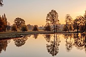 COTTESBROOKE HALL AND GARDENS, NORTHAMPTONSHIRE: SPRING, APRIL, VIEW OF PARKLAND, LAKE FROM THE MITCHELL BRIDGE, SUNRISE, REFLECTED, REFLECTIONS