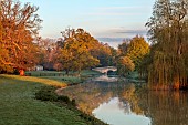 COTTESBROOKE HALL AND GARDENS, NORTHAMPTONSHIRE: SPRING, APRIL, VIEW OF PARKLAND, LAKE, BRIDGE FROM THE MITCHELL BRIDGE, SUNRISE, REFLECTED, REFLECTIONS