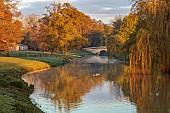 COTTESBROOKE HALL AND GARDENS, NORTHAMPTONSHIRE: SPRING, APRIL, VIEW OF PARKLAND, LAKE, BRIDGE, FROM THE MITCHELL BRIDGE, SUNRISE