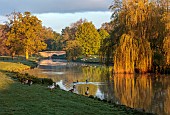 COTTESBROOKE HALL AND GARDENS, NORTHAMPTONSHIRE: SPRING, APRIL, VIEW OF PARKLAND, LAKE, BRIDGE, FROM THE MITCHELL BRIDGE, SUNRISE