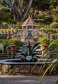 TRESCO ABBEY GARDEN, ISLES OF SCILLY: MAY, SPRING, VIEW PAST THE MEDITERRANEAN GARDEN TO THE SHELL HOUSE, AGAVE FOUNTAIN