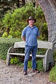 TRESCO ABBEY GARDEN, ISLES OF SCILLY: MAY, SPRING, PATH, HEAD GARDENER ANDREW LAWSON BESIDE A CUPRESSUS MACROCARPA, MONTEREY CYPRESS