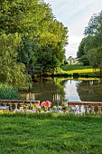 PRIORS MARSTON, WARWICKSHIRE, THE MANOR HOUSE: LONG WOODEN TABLE SET FOR DINNER ON BALCONY BESIDE THE LAKE, MAY