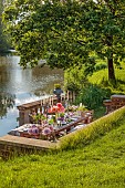 PRIORS MARSTON, WARWICKSHIRE, THE MANOR HOUSE: LONG WOODEN TABLE SET FOR DINNER ON BALCONY BESIDE THE LAKE, MAY