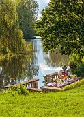 PRIORS MARSTON, WARWICKSHIRE, THE MANOR HOUSE: LONG WOODEN TABLE SET FOR DINNER ON BALCONY BESIDE THE LAKE, MAY
