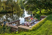 PRIORS MARSTON, WARWICKSHIRE, THE MANOR HOUSE: LONG WOODEN TABLE SET FOR DINNER ON BALCONY BESIDE THE LAKE, MAY
