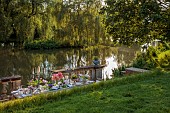 PRIORS MARSTON, WARWICKSHIRE, THE MANOR HOUSE: LONG WOODEN TABLE SET FOR DINNER ON BALCONY BESIDE THE LAKE, MAY