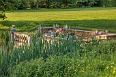 PRIORS MARSTON, WARWICKSHIRE, THE MANOR HOUSE: LONG WOODEN TABLE SET FOR DINNER ON BALCONY BESIDE THE LAKE, MAY