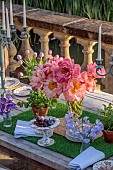 PRIORS MARSTON, WARWICKSHIRE, THE MANOR HOUSE: LONG WOODEN TABLE SET FOR DINNER ON BALCONY BESIDE THE LAKE, MAY, PEONIES