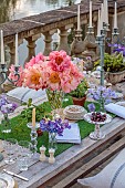 PRIORS MARSTON, WARWICKSHIRE, THE MANOR HOUSE: LONG WOODEN TABLE SET FOR DINNER ON BALCONY BESIDE THE LAKE, MAY, PEONIES
