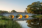 COTTESBROOKE HALL AND GARDENS, NORTHAMPTONSHIRE: THE MITCHELL BRIDGE, WATER, LAKE, SUNRISE, JUNE