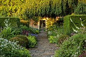 COTTESBROOKE HALL AND GARDENS, NORTHAMPTONSHIRE: THE TERRACE, ONOPORDUM ACANTHIUM, LUPIN MASTERPIECE, ALCHEMILLA MOLLIS, GERANIUM ORION, WALL, GATE, STONE URN