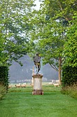 COTTESBROOKE HALL AND GARDENS, NORTHAMPTONSHIRE: STATUE IN THE SPINNEY GARDEN WITH SHEEP GRAZING BEYOND IN THE PARKLAND