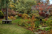 YORK GATE GARDEN, YORKSHIRE: AUTUMN, FALL, THE POND GARDEN, WATER, TREES, FOLIAGE, LAWN, METAL CONTAINER, TREE SEAT, BENCH