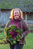 WOLLERTON OLD HALL, SHROPSHIRE: HEAD GARDENER CLAIRE TATLER HOLDING WREATH, CORNUS SIBERICA, THUJA OCCIDENTALIS, ILEX X ALTACLERENSIS