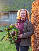 WOLLERTON OLD HALL, SHROPSHIRE: HEAD GARDENER CLAIRE TATLER HOLDING WREATH, CORNUS SIBERICA, THUJA OCCIDENTALIS, ILEX X ALTACLERENSIS