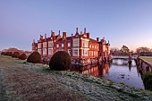 HELMINGHAM HALL GARDENS, SUFFOLK: WINTER, FROST, JANUARY, THE HALL AND MOAT WITH CLIPPED TOPIARY YEW