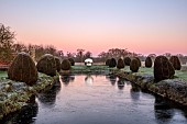 HELMINGHAM HALL GARDENS, SUFFOLK: WINTER, FROST, JANUARY, MOAT, CLIPPED TOPIARY YEW, DAVID HARBER SUNDIAL, REFLECTED, REFLECTIONS