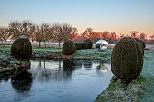 HELMINGHAM HALL GARDENS, SUFFOLK: WINTER, FROST, JANUARY, MOAT, CLIPPED TOPIARY YEW, DAVID HARBER SUNDIAL, REFLECTED, REFLECTIONS