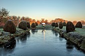 HELMINGHAM HALL GARDENS, SUFFOLK: WINTER, FROST, JANUARY, MOAT, CLIPPED TOPIARY YEW, DAVID HARBER SUNDIAL, REFLECTED, REFLECTIONS