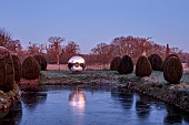HELMINGHAM HALL GARDENS, SUFFOLK: WINTER, FROST, JANUARY, MOAT, CLIPPED TOPIARY YEW, DAVID HARBER SUNDIAL, REFLECTED, REFLECTIONS